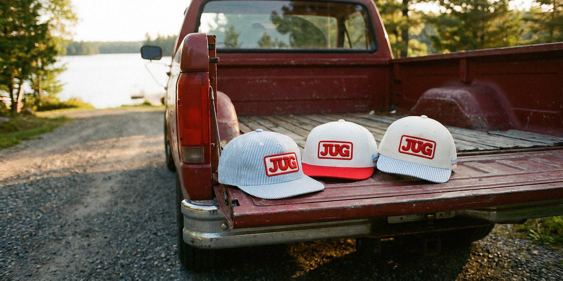 The three JUG hats LTD Customs built, the JUG Delivery Hat, JUG Red Top Hat and JUG Delivery Brim, on the tailgate of a red pickup by a Muskoka lake